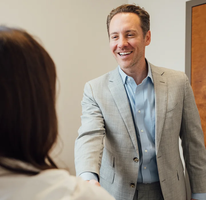 A bright, close-up shot of Dr. Fournier smiling warmly as he shakes hands with a patient, conveying a sense of trust and successful results.
