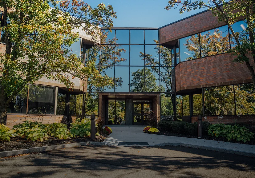 A wide, clear exterior shot of the Fournier Plastic Surgery building, featuring a modern brick and glass facade surrounded by autumn trees and professional landscaping.