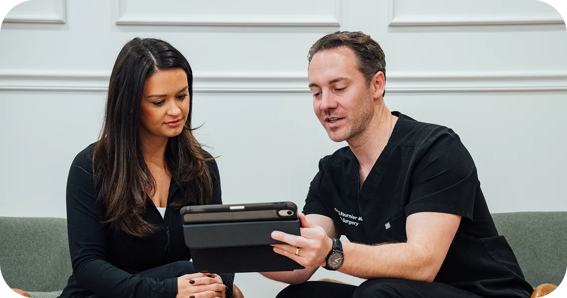 Dr. Fournier, dressed in black clinical scrubs, sits with a patient in a comfortable lounge area while sharing information on a digital tablet.