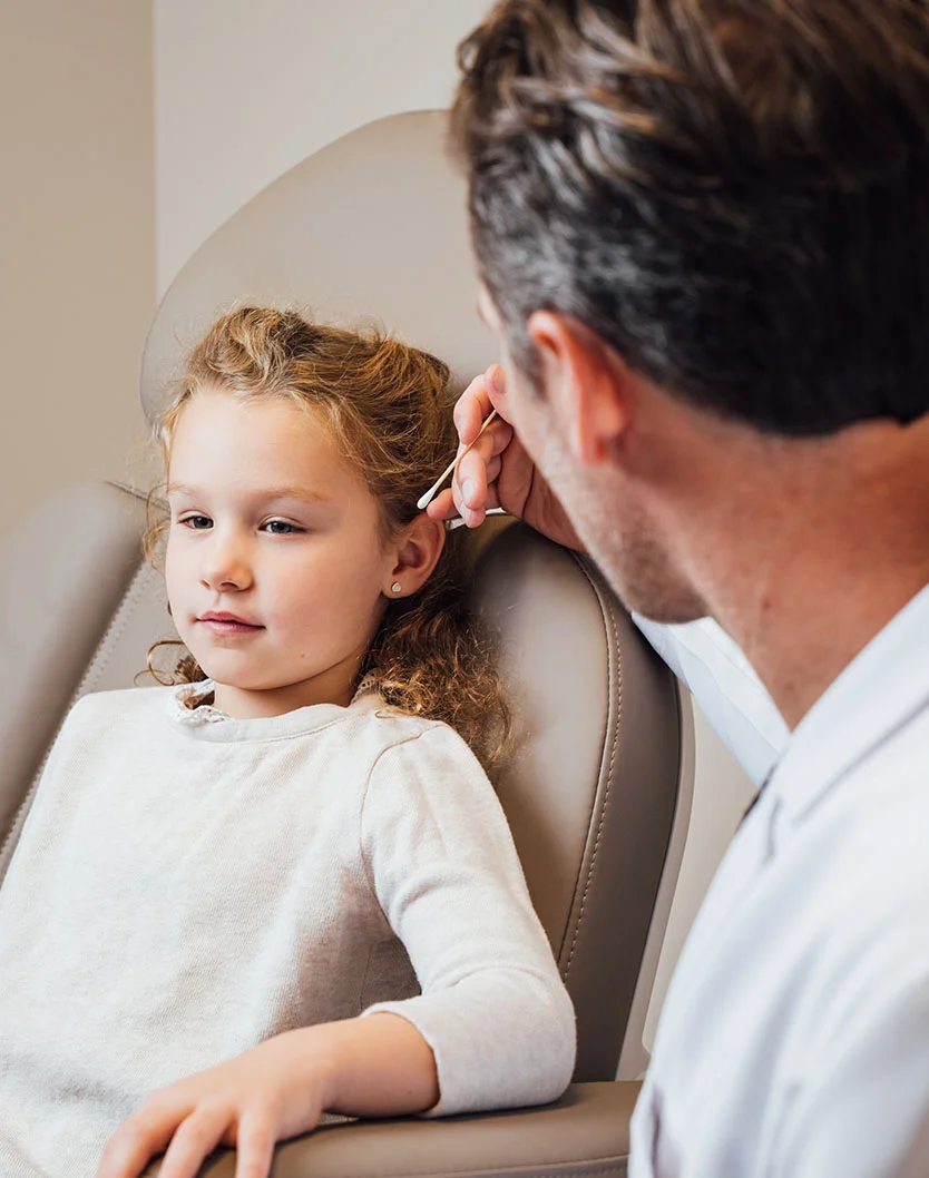 A side-view of Dr. Fournier carefully examining a young patient's ear during a clinical consultation.
