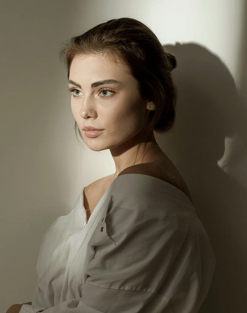Profile view of a woman with her hair in a bun, looking to the side as natural light highlights her facial profile and bridge of the nose.