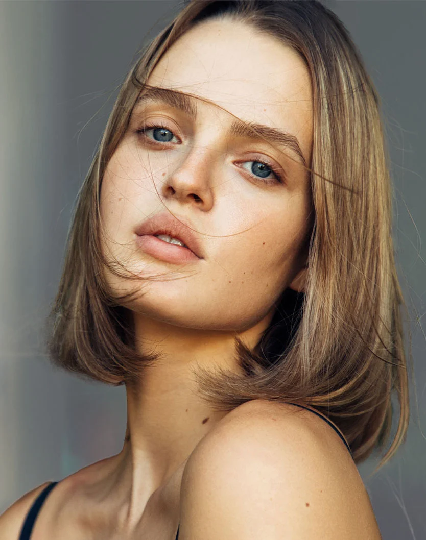 Close-up portrait of a woman with blonde hair and blue eyes, featuring a natural, soft lip aesthetic.