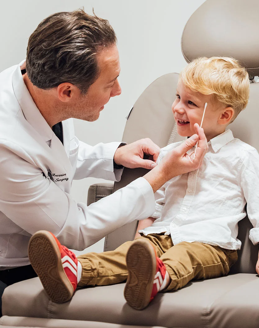 Dr. Fournier in a white lab coat uses a medical swab to examine a young girl's forehead during a clinical appointment.