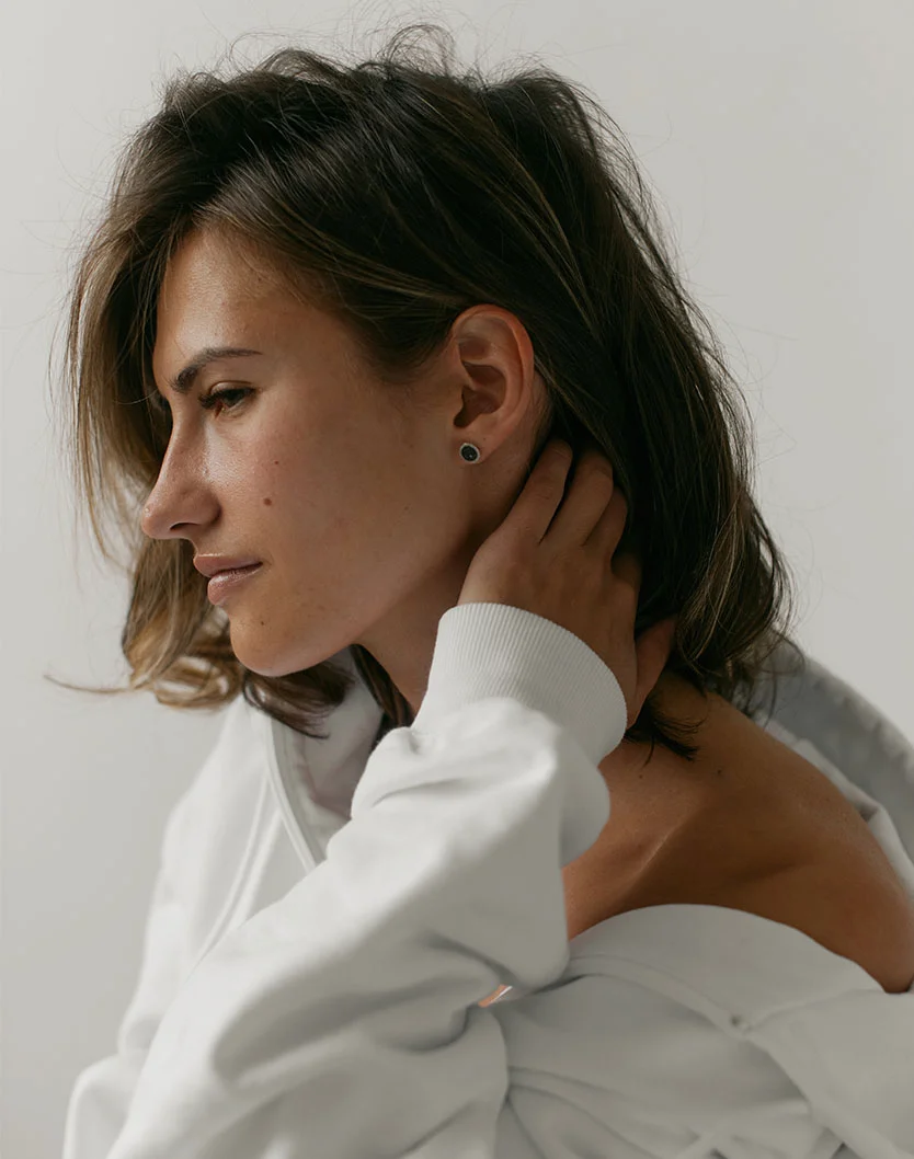 A profile shot of a woman with short brown hair wearing a white sweatshirt, looking downward.